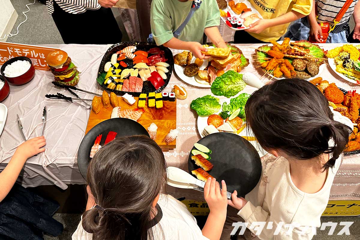 樹脂とろうで作られた食品のサンプルでバイキング遊びをする子供
