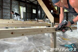 中古住宅のリノベーション現場で、床下の根太を施工する職人の作業風景。断熱対策のための基礎工事