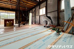 木造住宅の床下に断熱材と気密シートを敷設する作業を行う職人の様子