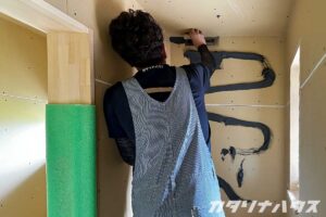 壁面タイル施工のため、下地に黒色の接着剤を塗布している作業風景。DIYリノベーションの一場面