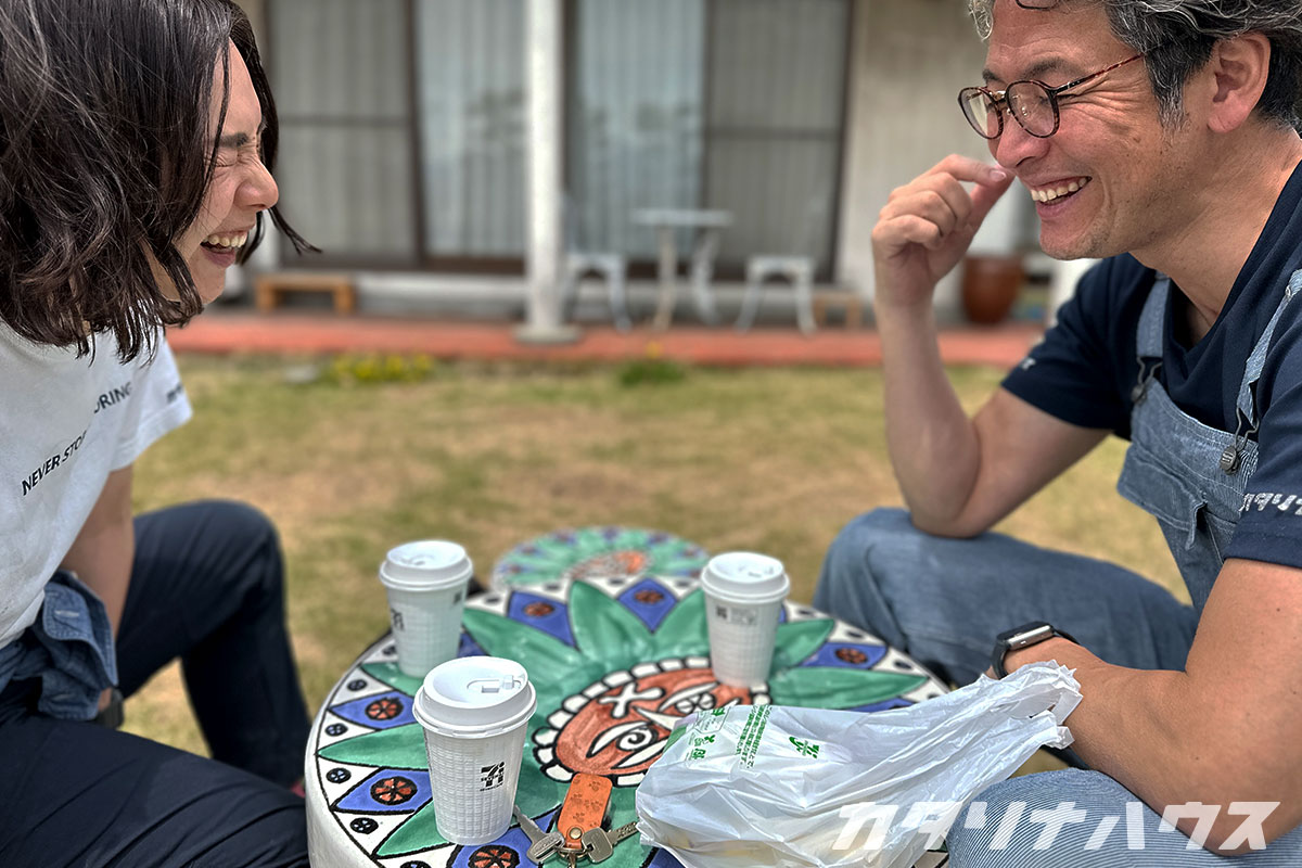 リノベーション現場の庭先でコーヒーブレイクを楽しむスタッフ。和やかな雰囲気の中で談笑する様子