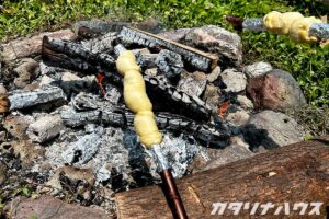 焚き火の上で棒に巻きつけたパン生地を焼いているアウトドアクッキングの様子