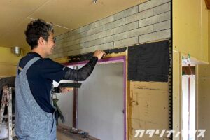 室内の壁に接着剤を塗りながらタイルを貼っている職人の作業風景