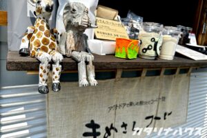 動物の木彫り人形や手作り雑貨、コーヒー豆が並ぶクラフトマーケットのブース 画像4：焚き火でパンを焼く子ども