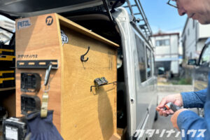 軽バンの荷室カスタムでサイド収納を製作中。木製パネルにフックと金具を取り付ける様子。