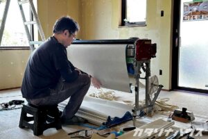 クロス貼り作業の準備をする職人。機械に壁紙をセットして施工の準備をしている。