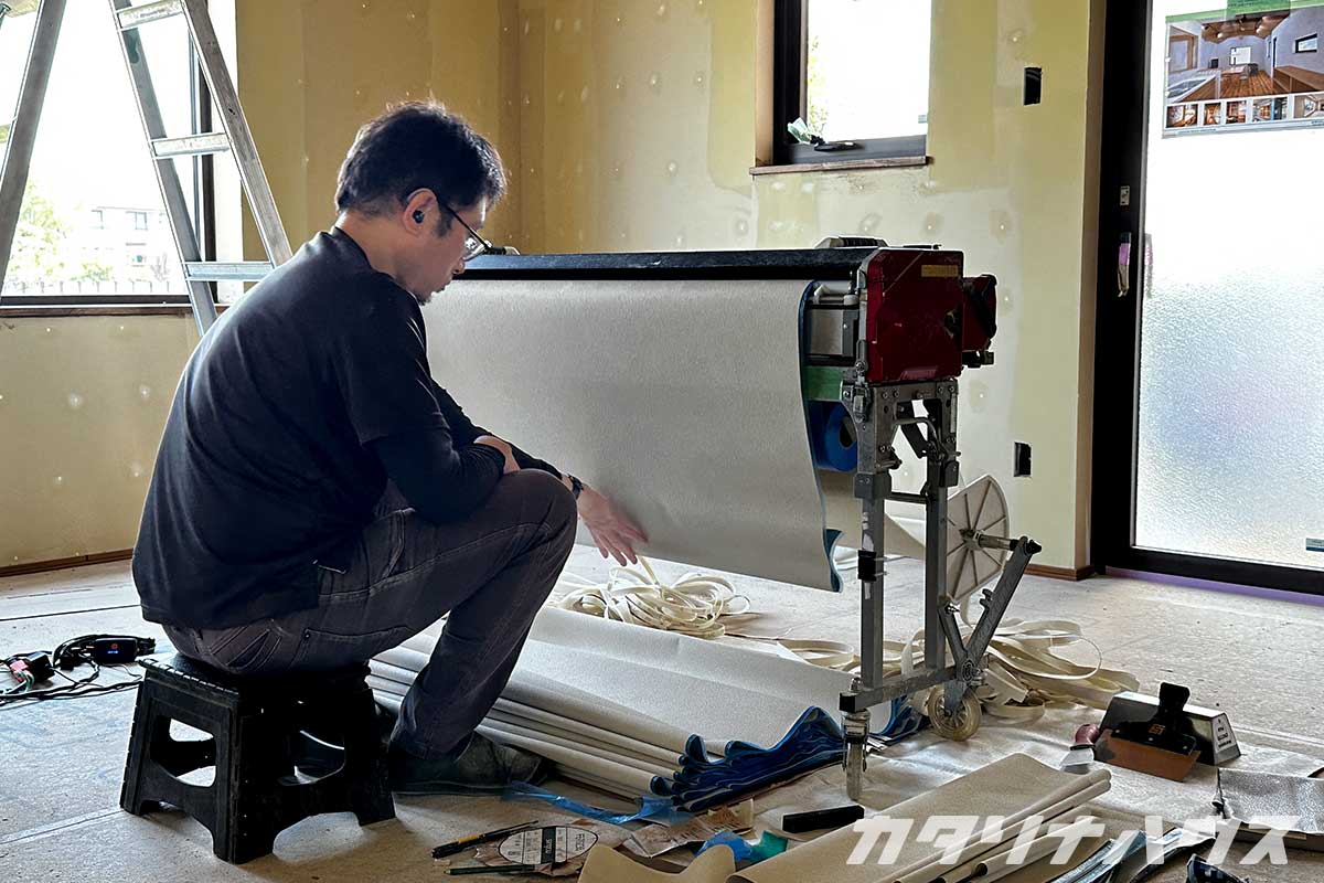 クロス貼り作業の準備をする職人。機械に壁紙をセットして施工の準備をしている。