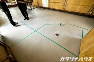 床に緑色のマスキングテープで間取りを示しながら打合せをする職人とスタッフの様子