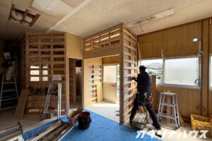 間仕切り壁の骨組みが組まれ、職人が木材の取り付け作業をしている店舗内の様子