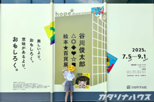 谷川俊太郎の絵本展の大きな看板の前でポーズをとる女の子