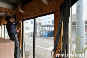 白い暖簾を撤去し、窓の寸法を測る男性職人
