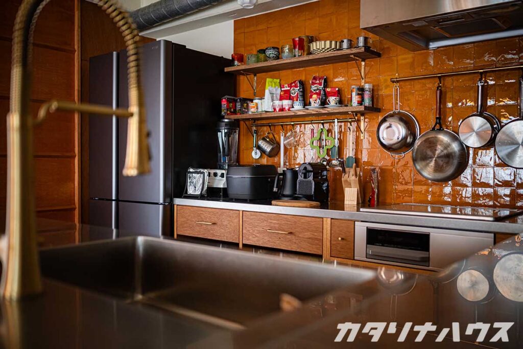 黄色いクラフトタイルが貼られたキッチンバック。様々な調理器具や食品がディスプレイ棚に飾られている。
