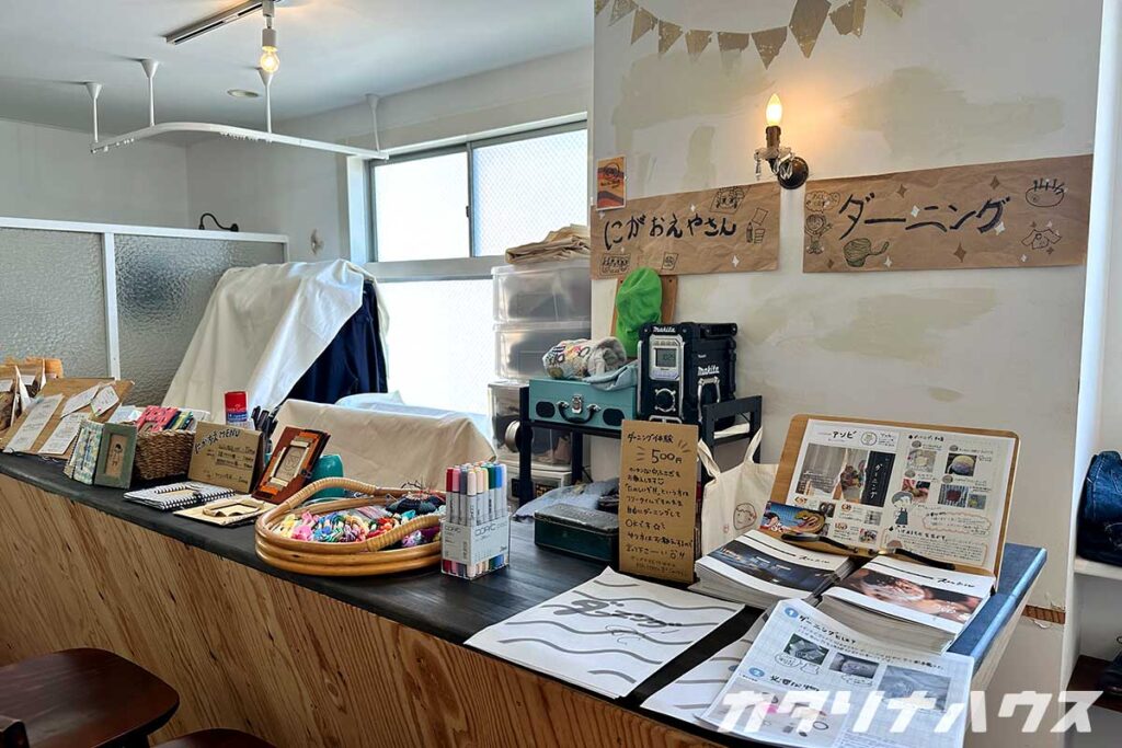 ダーニングのワークショップと似顔絵屋さんの手作り看板が並ぶブース。ダーニングの説明テキストやカラフルな糸が並ぶ。
