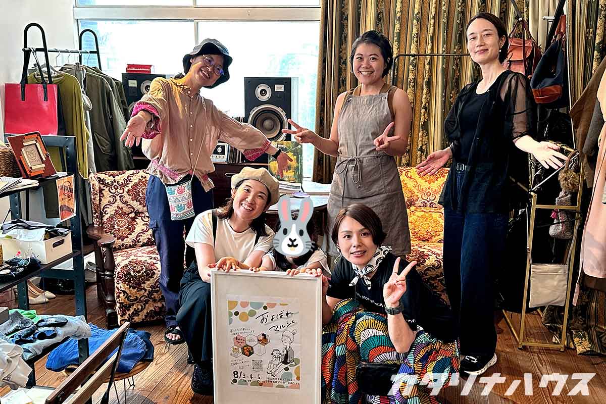 およばれマルシェの出展者集合写真。看板を中心に５人の女性が並んでいる。