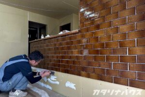 キッチン腰壁にブラウンタイルを貼り付ける施工中の風景。目地を整えながら丁寧に仕上げている作業の様子