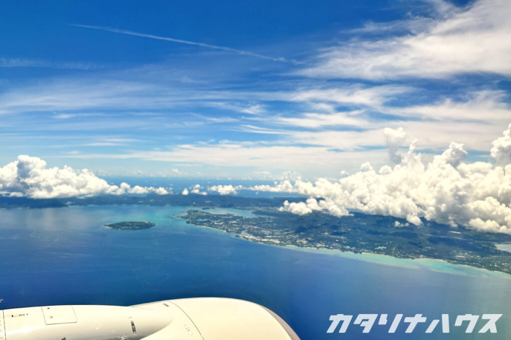 飛行機の窓から見下ろした沖縄の海と島々。エメラルドグリーンの海と青い空、白い雲が広がる絶景