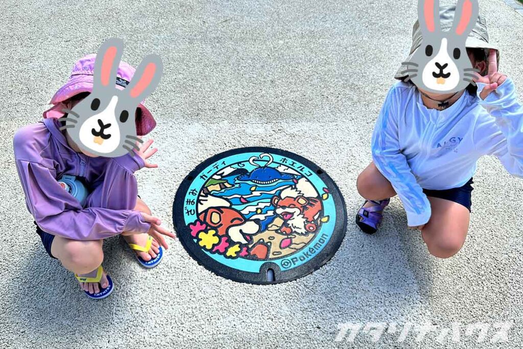 座間味島のポケモンマンホール『ポケふた』。ガーディとホエルコが描かれており、子どもたちが記念撮影