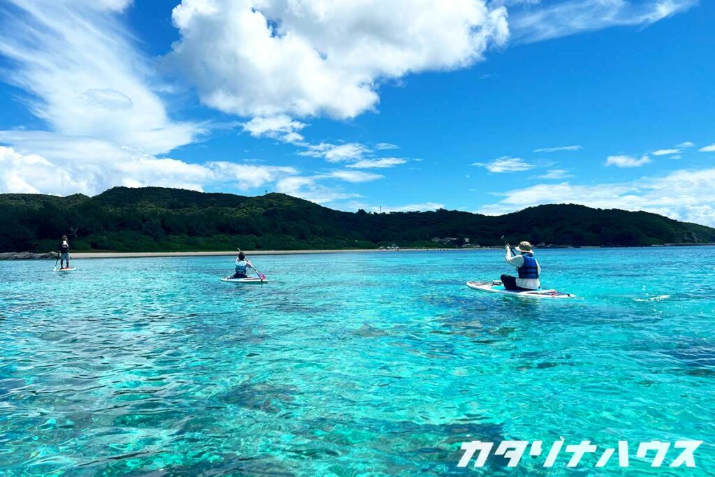 透明度抜群の海の上でSUPを楽しむ家族。座間味島の穏やかな海でパドルを漕ぐ様子