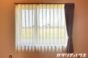 片開きのカーテンとレースカーテン。レースカーテンからはうっすらと窓外の田園が見える。