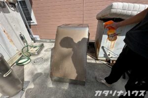油とホコリで汚れたレンジフード。これから掃除をするスタッフの右手にはオレンジのクレンザーが握られている。
