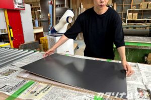 黒いメラミンボードを補強された下地に貼り付ける女性