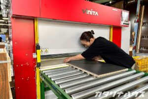 ローラーがついた圧着機にメラミンボードを張り付けたパネルを乗せる職人