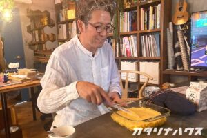 本が並ぶ収納棚の前でスイートポテトの表面をヘラでならす男性。