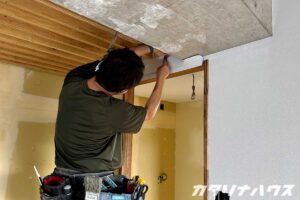 男性職人が天井近くのクロス端を仕舞している。天井はコンクリート表し。