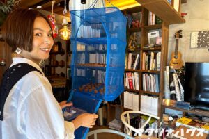 青い干しかごに干された梅干を前に笑顔の女性スタッフ