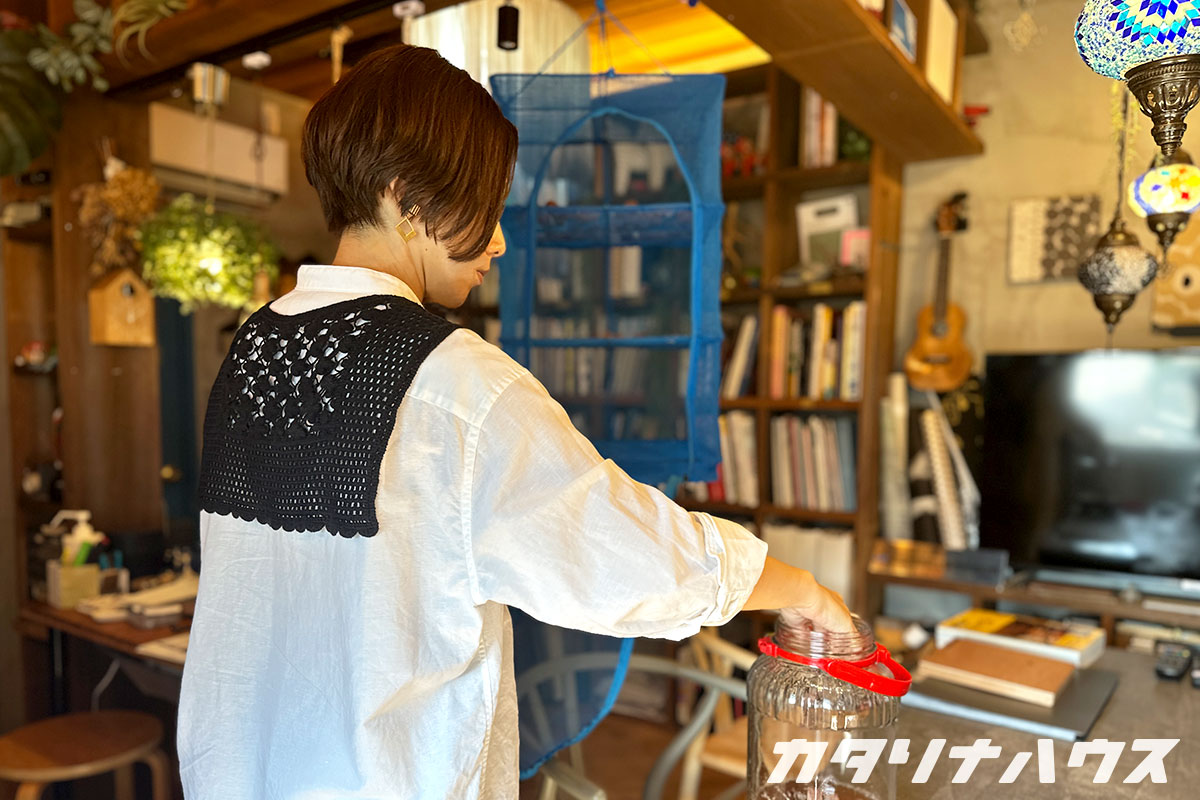 吊るされた干しかごから梅干をビンに移すスタッフ
