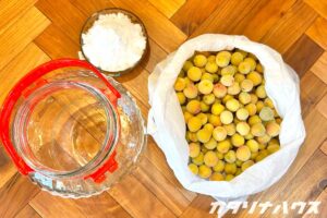 ヘリンボーンの板の上に準備された梅干の準備物。果実酒ボトルと冷凍された小梅と塩