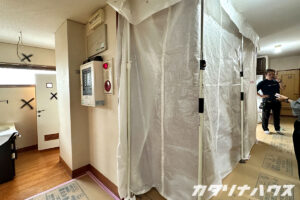 リノベーション工事のために養生と養生用シートが設置された廊下。壁には解体予定を示す印も入り、着工前の準備が進む現場の様子が伝わります。