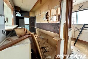 解体作業が進むキッチンで、壁材やカウンターが取り外され、内部の下地や配線が露出しているリノベーション現場。撤去された木材や廃材が床に積まれた施工中の様子。