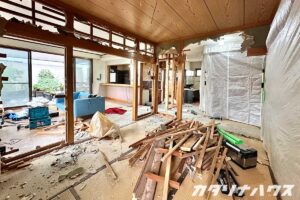 壁や柱の解体が進む室内で、木材の廃材が大量に積まれ、床には石膏ボードの破片が散らばるリノベーション現場。和室とリビングの仕切りを撤去中の施工途中の様子。