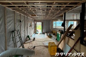 中古住宅リノベーションの施工現場。天井下地の木組みや壁の断熱材が施工され、配線工事や床下地づくりが進む室内の様子