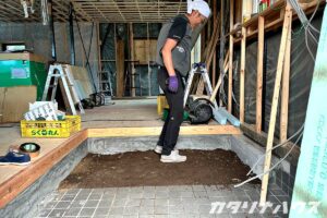 中古住宅リノベーションの現場で、玄関土間部分の土を整地している職人。床下断熱材を敷き込む前の下準備作業