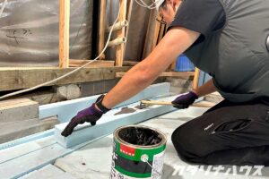 玄関土間の立ち上がり部分にスタイロフォームを固定するため、防水性のある接着材を塗り広げる職人の作業シーン。断熱補強を行うリノベーション工事