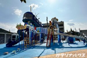 青い海をテーマにした巨大な複合遊具が設置された公園で、すべり台やロープ遊具などが揃うカラフルな遊び場の全景。子どもたちが遊べる海中デザインのアスレチック遊具。