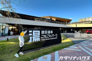湯田温泉こんこんパークの大きな黒い立体看板と、モダンな建物の外観。入口前の足湯広場から湯気が立ちのぼる、温泉地のランドマーク的スポット。