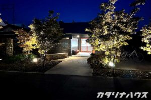 夜間にライトアップされた建物のエントランスと植栽が映る景観。アプローチ周りの木々が照明で照らされ、落ち着いた雰囲気の外観。