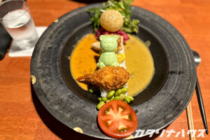くま型の最中がのった創作カレー料理で、揚げ物や野菜が彩りよく盛り付けられたプレート。