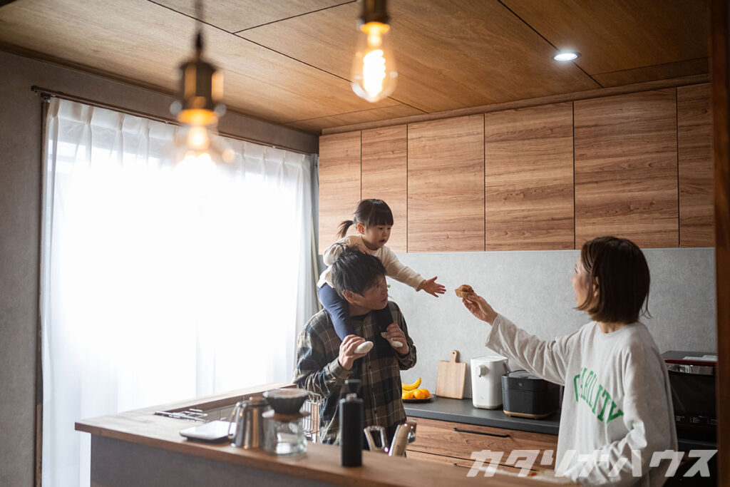 リノベーションされたキッチンで過ごす家族。お父さんに肩車された女の子がお母さんからお菓子を受け取る様子