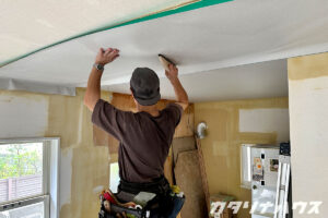 天井に貼ったクロスをヘラですり気泡を抜く職人の後ろ姿