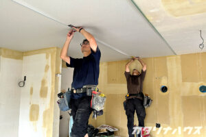 内装工事に入る二人の男性職人。天井のクロスの継ぎ目を抑えている