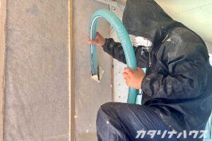 専用のホースを使って木繊維の断熱材を壁に詰め込んでいく男性スタッフ