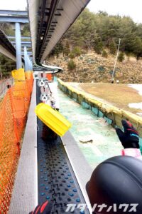 初心者用リフトで坂の頂上を目指す親子。手には黄色いソリを持っている。