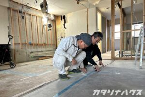 リノベーション現場で、床にしゃがみ込みながら寸法を確認している職人とスタッフ