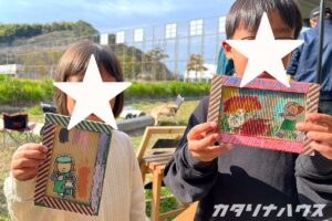 作ったカラフルなポストカードを手に作品を披露する兄妹。