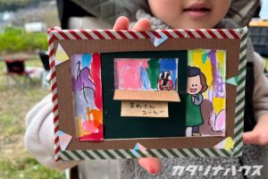 ひょっこり顔を出す女の子のイラストが描かれたポストカードにデコレーションをした子供